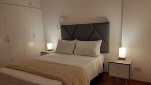 Um quarto com cama, mesas de cabeceira, guarda-roupa e cabeceira.