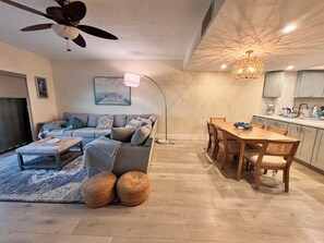 A modern living room with a sofa, coffee table, and two large woven baskets. There is a dining area with a wooden table and chairs. - Waterfront Longboat Key Retreat With Dream Views (Longboat Key)
