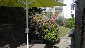 Zona de pati amb taula i cadires, un parasol groc i un paviment de pedra.
