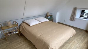 Un dormitori amb un llit, sòl de fusta, una petita taula de nit, una prestatgeria penjada a la paret i una finestra amb persianes.
