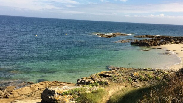 Paisatge costaner amb aigües clares, roques i una platja de sorra.