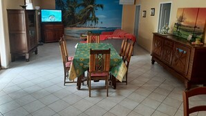 Comedor con una mesa preparada para cuatro personas, un televisor y un mural con una escena de playa.