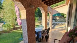 Un patio cubierto con una mesa, sillas, una planta en maceta y vistas al jardín circundante.