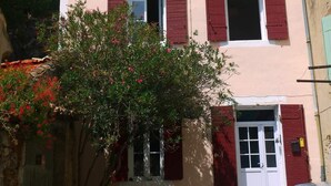 Un edificio con contraventanas rojas, una torre de piedra y un jardín con plantas en flor.