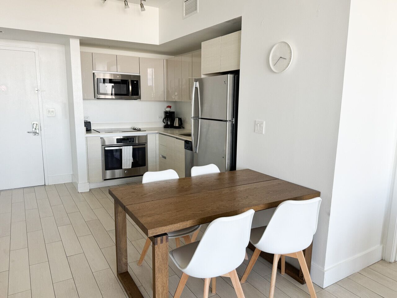 A modern kitchen with white cabinets, stainless steel appliances, and a wooden dining table with white chairs.