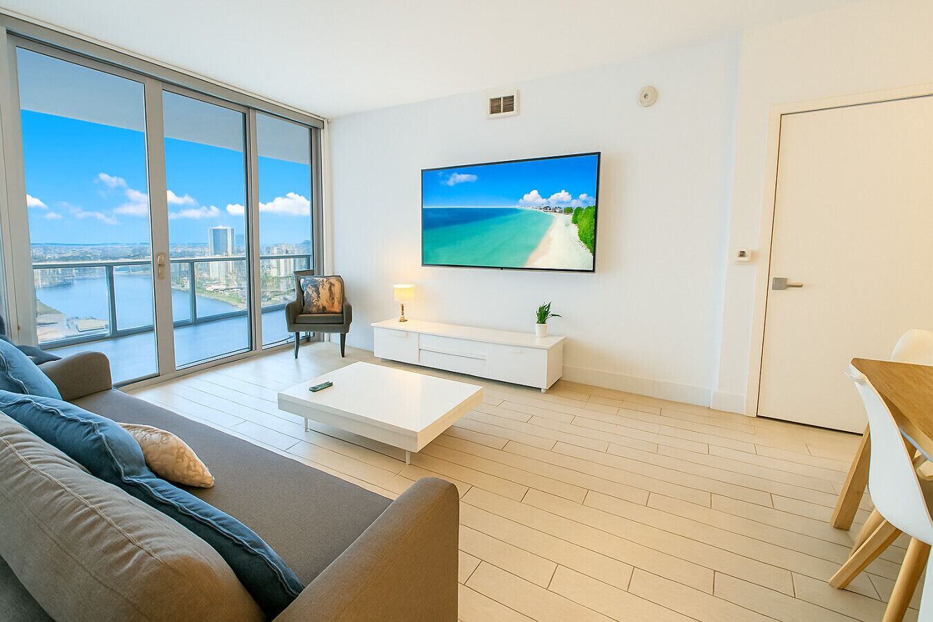 A modern living room with a large window, a flat-screen TV, a sofa, a coffee table, and a small side table.