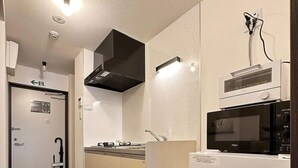A compact kitchen with a microwave, stove, and built-in oven. There is a sink with a faucet, and a black range hood above the stove. - Nagomi by b hotel | Comfortable Studio Stay N22 (Hiroshima)