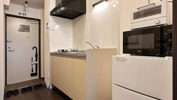 A compact kitchen with a microwave, stove, and built-in oven. There is a sink with a faucet, and a black range hood above the stove.