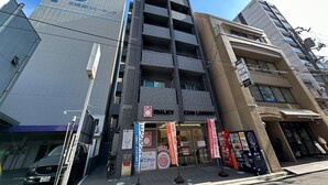 A multi-story building with a parking sign, a coin laundry, and various commercial establishments. - Nagomi by b hotel | Comfortable Studio Stay N22 (Hiroshima)