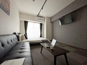 Una moderna camera d'albergo con divano, un letto, una televisione a schermo piatto montata a parete e un portatile su un tavolino.