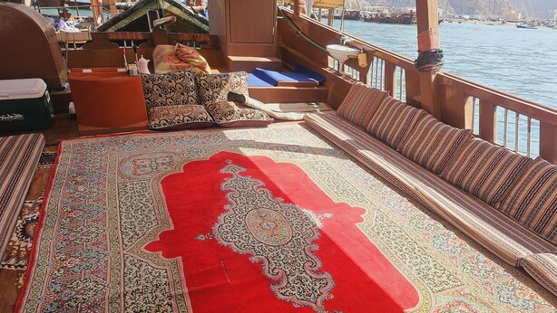 Un pont de bateau agrémenté d’une grande moquette rouge, de sièges en bois et offrant une vue sur l’eau.