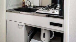 A compact kitchenette with a sink, stove, microwave, and storage shelves. - Homey w/ 1BR in Onomichi for 3 Ppl (Onomichi)