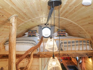 A cozy attic bedroom with a sloped ceiling, a circular skylight, two beds with patterned bedding, a hanging light fixture, and a wooden bench. - Erme (Plymouth)