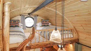 A cozy attic bedroom with a loft bed, a small window, and a wooden staircase.
