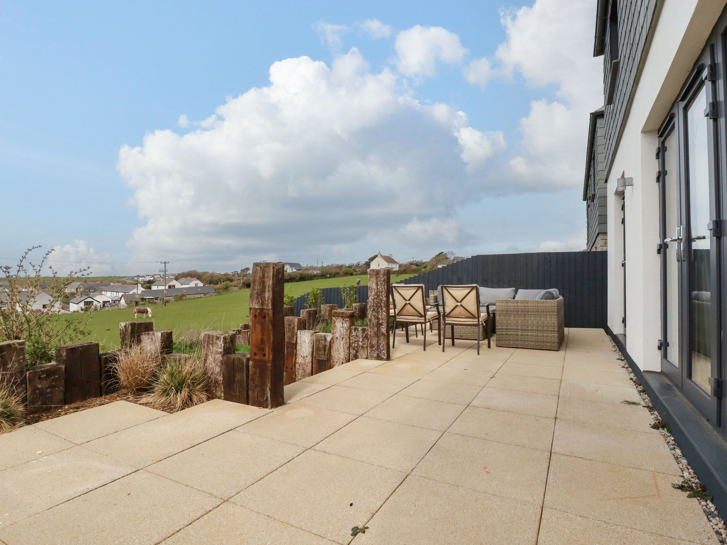 A patio area with a view of a green field and houses in the distance.