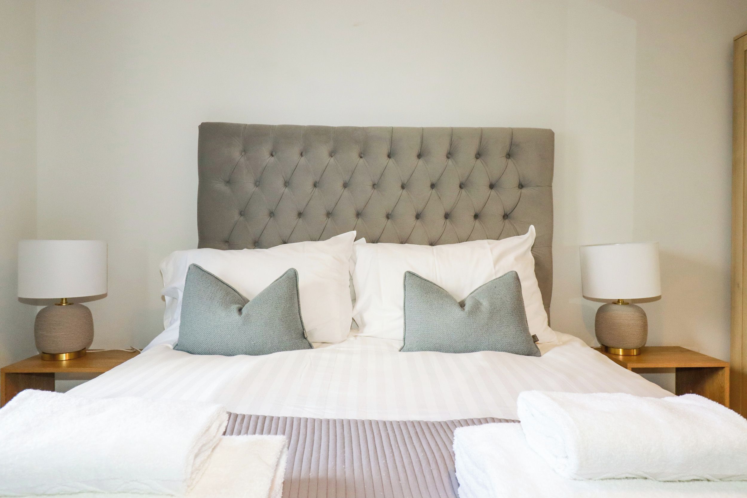 Een net opgemaakt bed met een gestuufd hoofdbord, twee bedlampen en twee kussens.