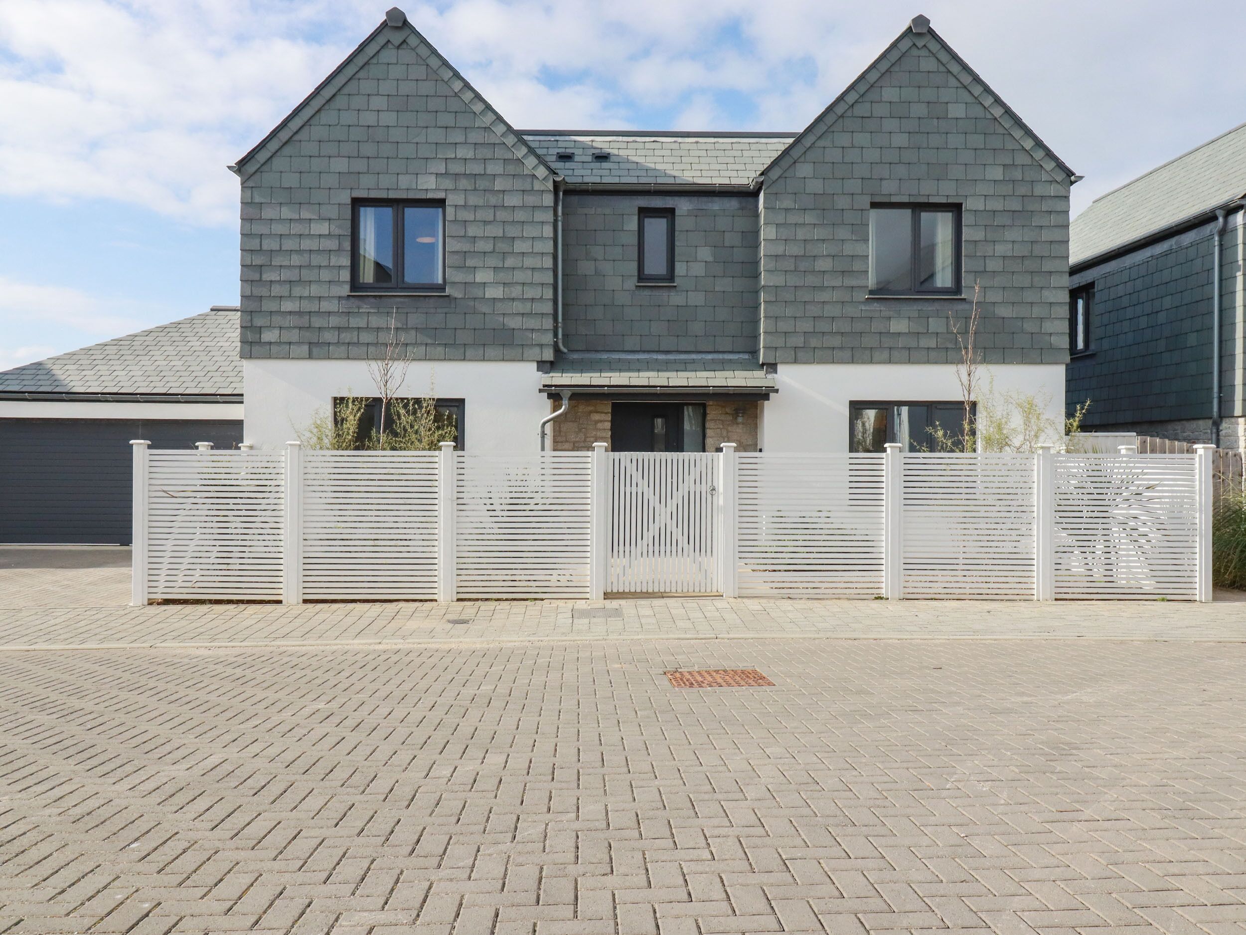 A two-story house with a grey roof, white exterior walls, and a white fence.