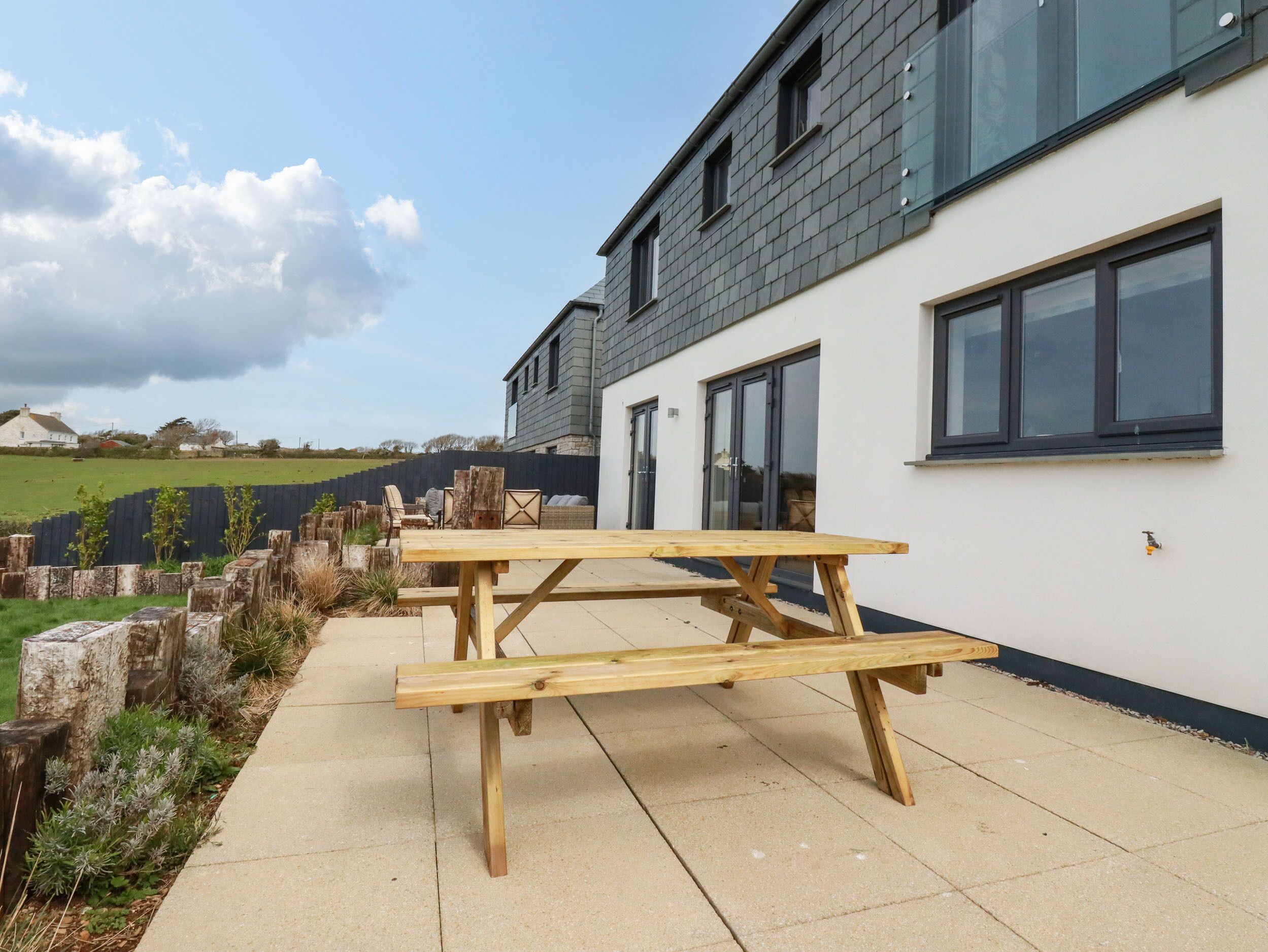 An outdoor wooden picnic table set up on a patio with a white building in the background.