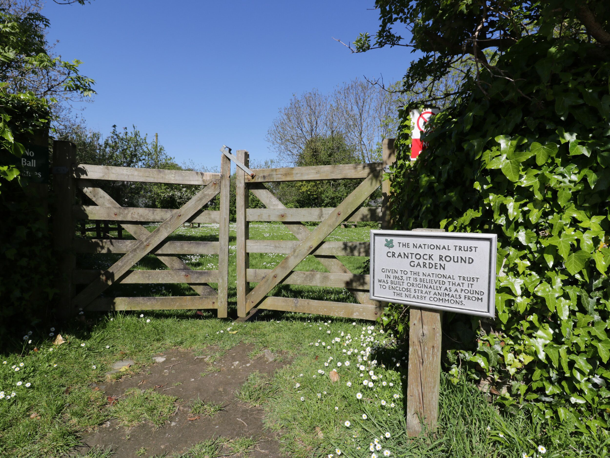 Una puerta de madera con un cartel que indica Jardín Crantock Trust.