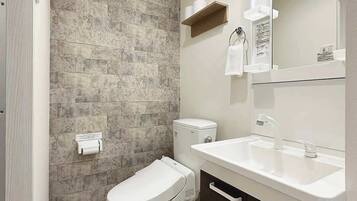Une salle de bain moderne avec un mur en pierre, des toilettes, un lavabo avec un miroir et un porte-serviettes.