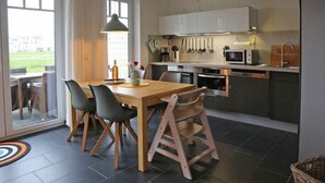 Et moderne køkken med spiseplads, med et træbord, sorte stole og en hængende lampe.