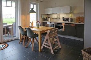 A modern kitchen with a dining area, featuring a wooden table, black chairs, and a hanging light fixture.