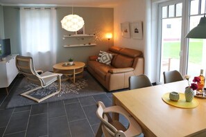 A modern living room with a leather sofa, a round coffee table, and a dining table with a vase of flowers. - Moderne Ferienwohnung Wellenreiter - 3 Min. vom Strand Entfernt (Börgerende-Rethwisch)