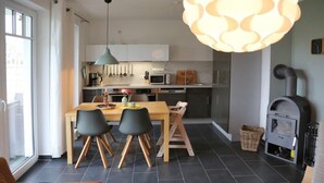 Et moderne køkken med spiseplads, med et stort bord, stole og en hængende lampe.