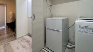 A compact laundry area with a washing machine and dryer, a door leading to a room with a piano, and a wooden floor.