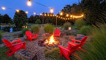 A fire pit with red chairs arranged around it, surrounded by a gravel area with greenery.
