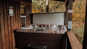 Ein Whirlpool mit Holzterrasse und Stuhl, umgeben von Bäumen.