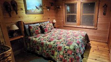 A cozy wooden cabin bedroom with a bed, a window with blinds, and wall decorations including animal heads.