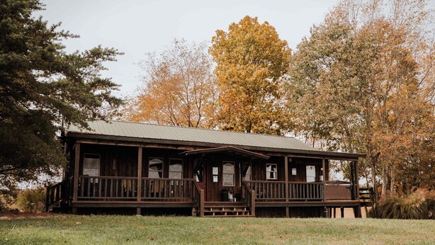 Eine rustikale Holzhütte mit Veranda, umgeben von Bäumen im Herbstlaub.