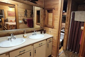 A wooden cabin-style bathroom with two sinks, a large mirror, and a shower area.