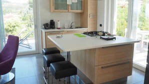 Une cuisine moderne dotée d’un îlot central, de tabourets de bar, d’une machine à café et offrant une vue sur la verdure environnante.