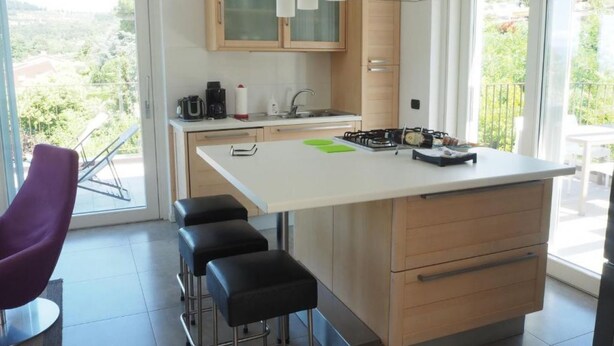 A modern kitchen with a central island, bar stools, a coffee machine, and a view of greenery outside. - Fair View Apartment, 1st Floor (Bardolino)