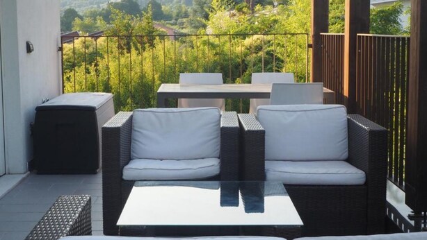 Un balcon agrémenté de meubles en osier, d’une table en verre et offrant une vue sur un paysage verdoyant.