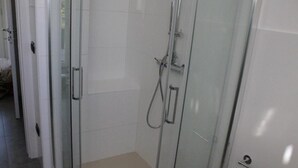 Un espace douche clos par des parois de verre, équipé d’un pommeau de douche à main et d’un robinet mural.