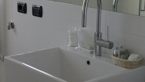 Une salle de bain avec un lavabo blanc, un miroir, un robinet et un panier contenant des articles de toilette.