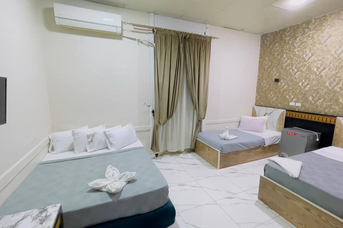 A hotel room with two beds, a flat-screen TV, an air conditioner, and a curtain.