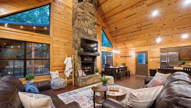 A cozy cabin interior with a stone fireplace, leather sofas, a dining area, and a kitchen. - Close to All~Mini Golf~Fire-Pit~Swing Set~Hot Tub (Broken Bow)