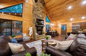 A cozy cabin interior with a stone fireplace, leather sofas, a dining area, and a kitchen.
