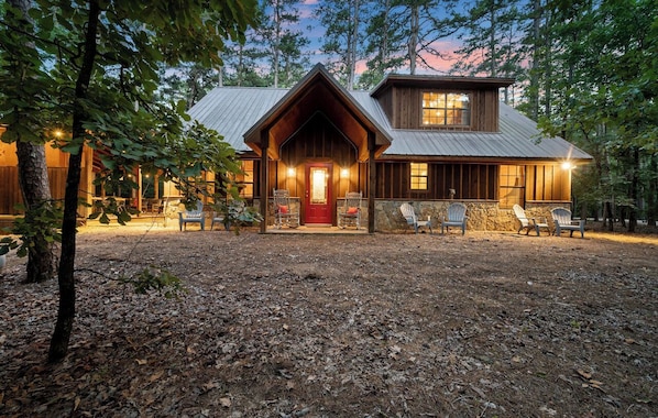A rustic cabin with a prominent front porch, stone steps, and multiple seating areas.