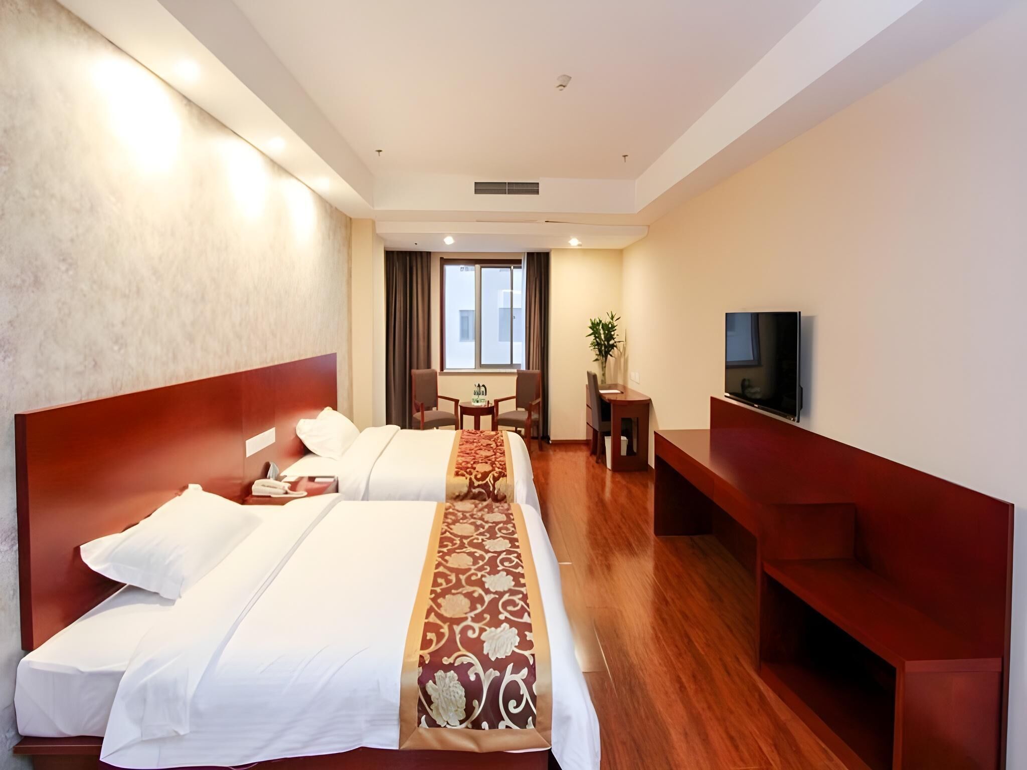 A hotel room with two beds, a TV, a desk, and a chair.