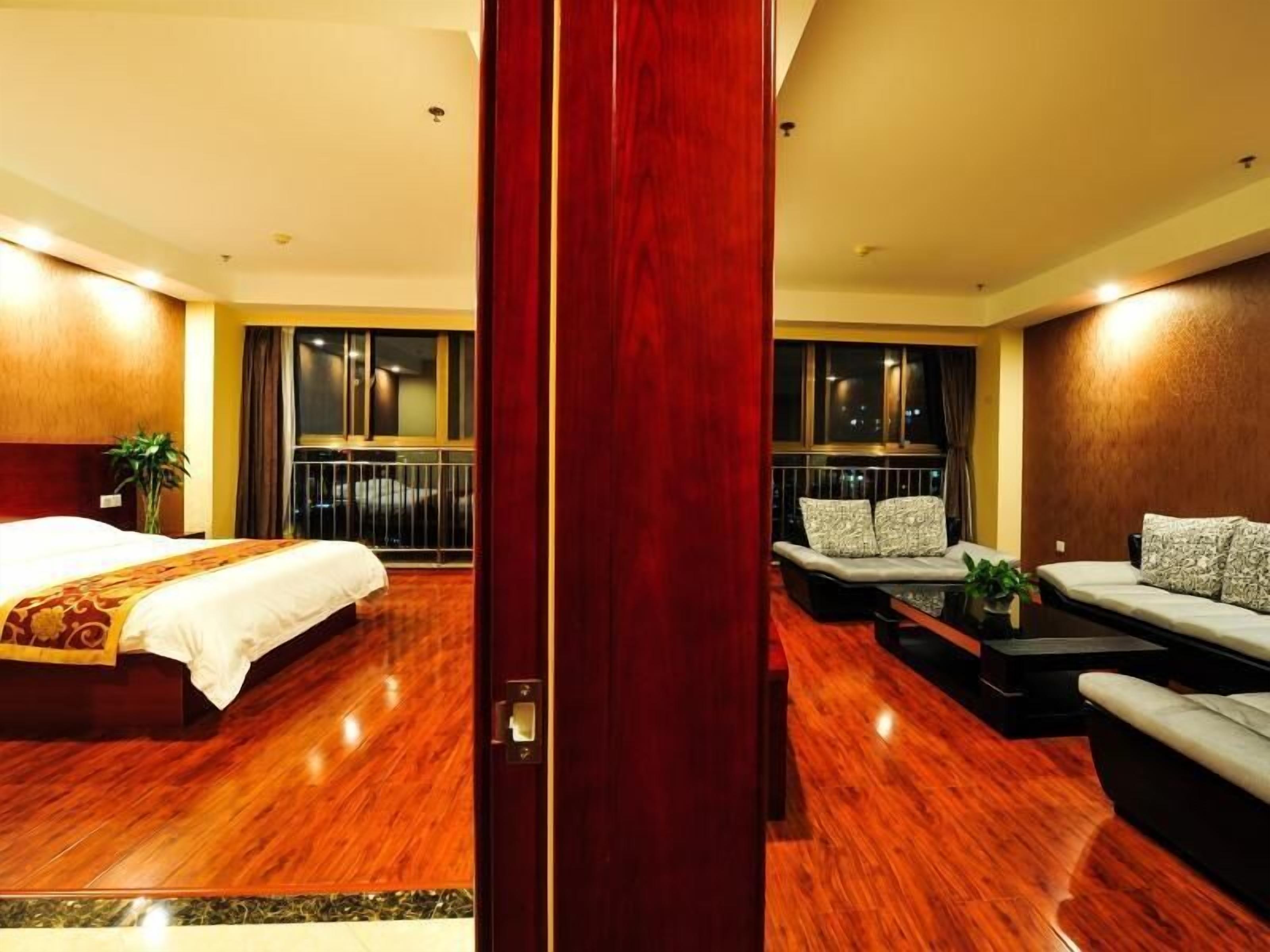 A hotel room with a bed, a sofa, a small table, and a balcony with a railing.