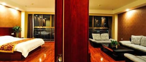 A hotel room with a bed, a sofa, a small table, and a balcony with a railing.