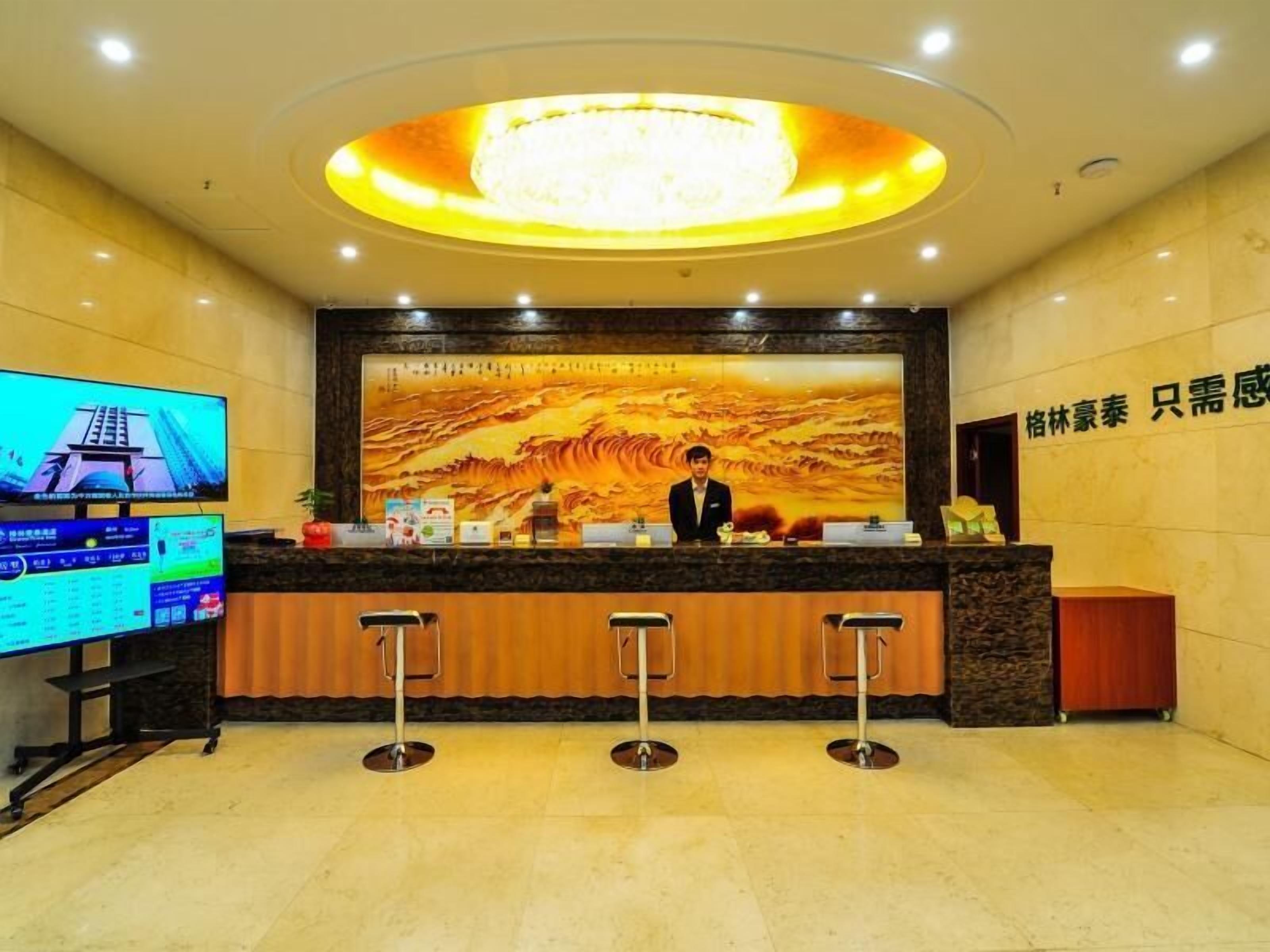 A hotel reception area with a large digital screen displaying a cityscape, a reception desk with a receptionist, and a bar area with stools.