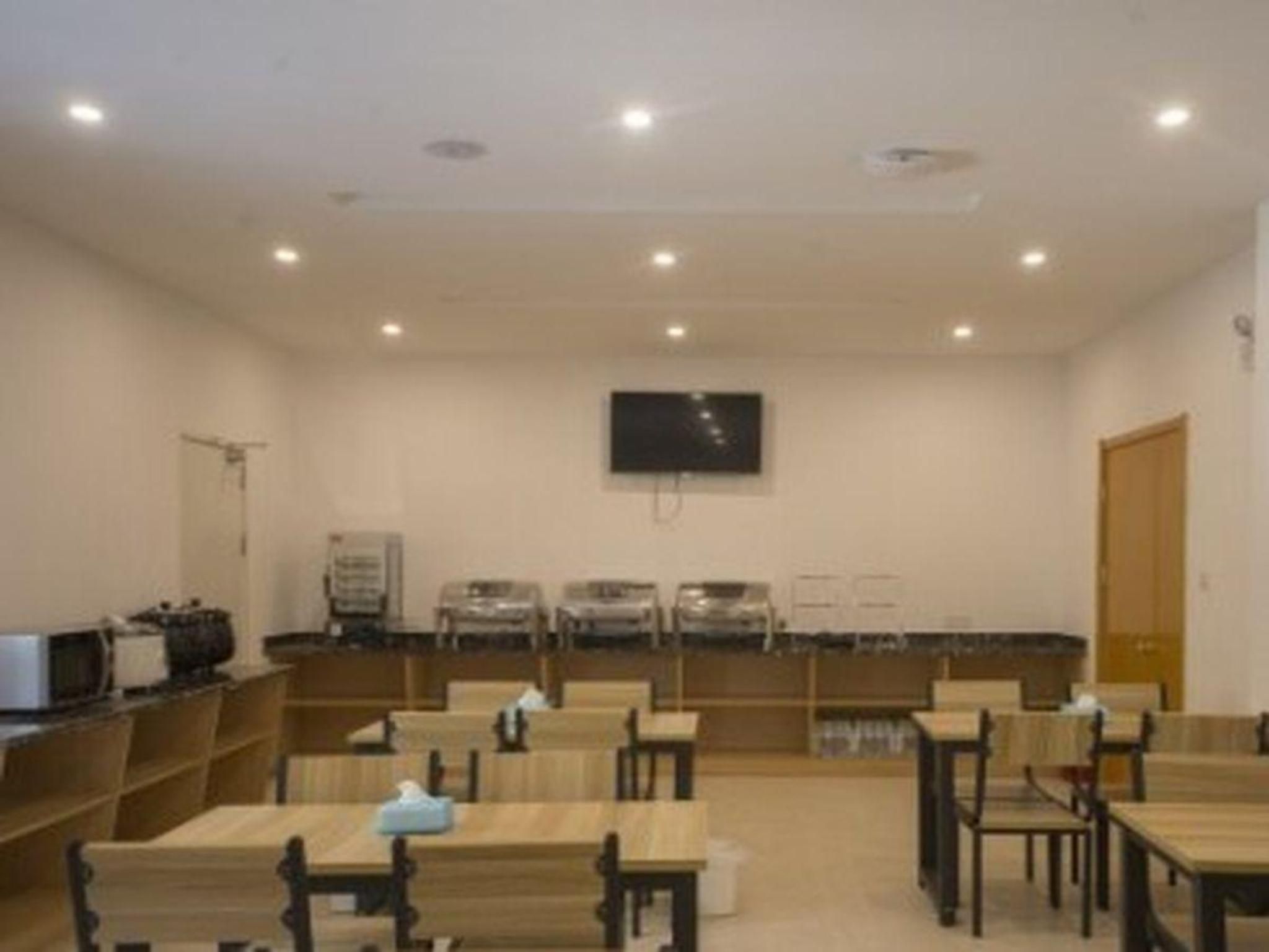 A room with tables and chairs arranged for dining, a flat-screen TV mounted on the wall, and a counter with appliances.