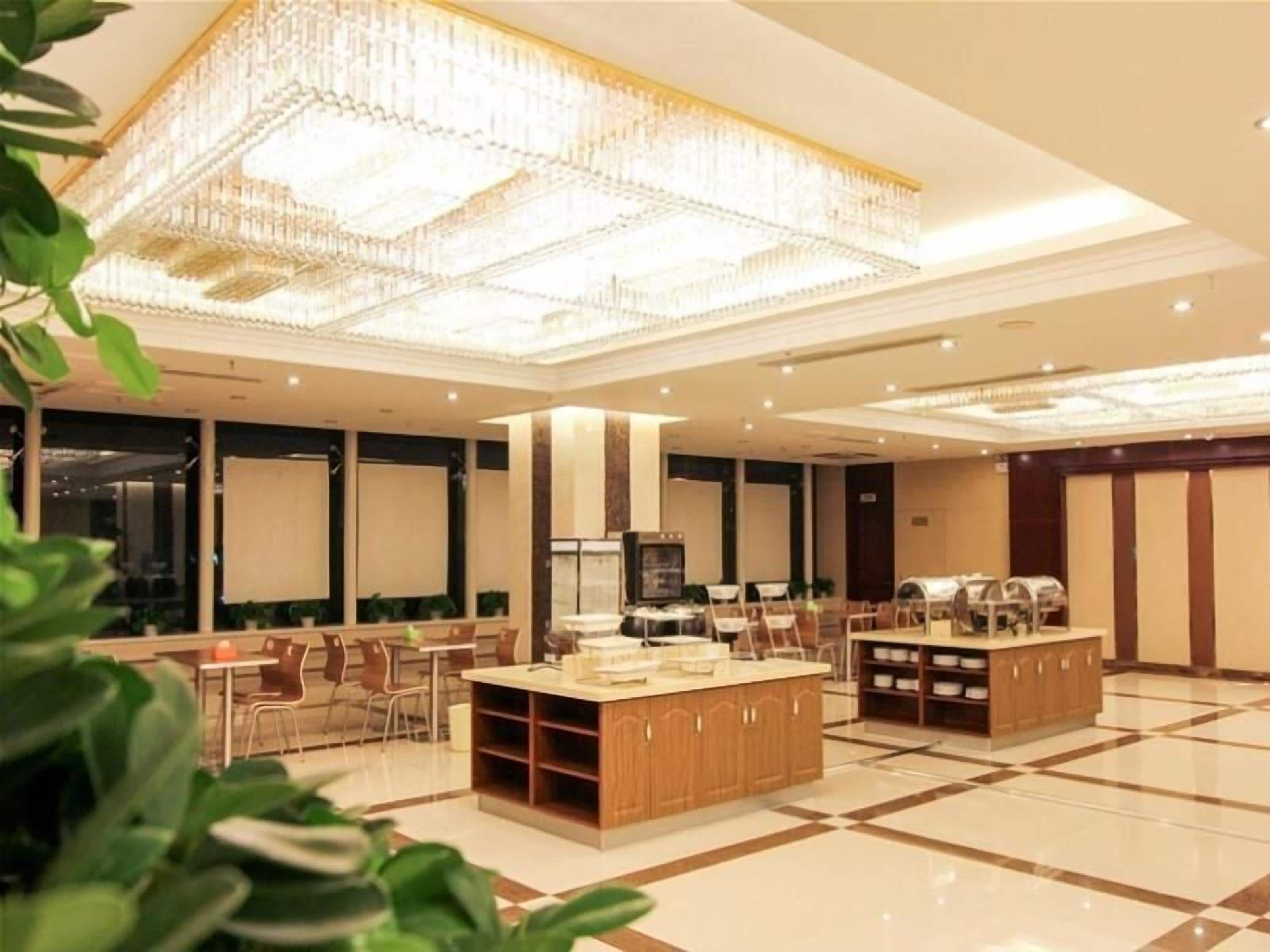 Een ruime hotellobby met een grote kroonluchter, een centraal gelegen receptiebalie en een zithoek met stoelen en tafels.