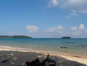 A beach with clear blue water, a sandy shore, and a small island in the distance.